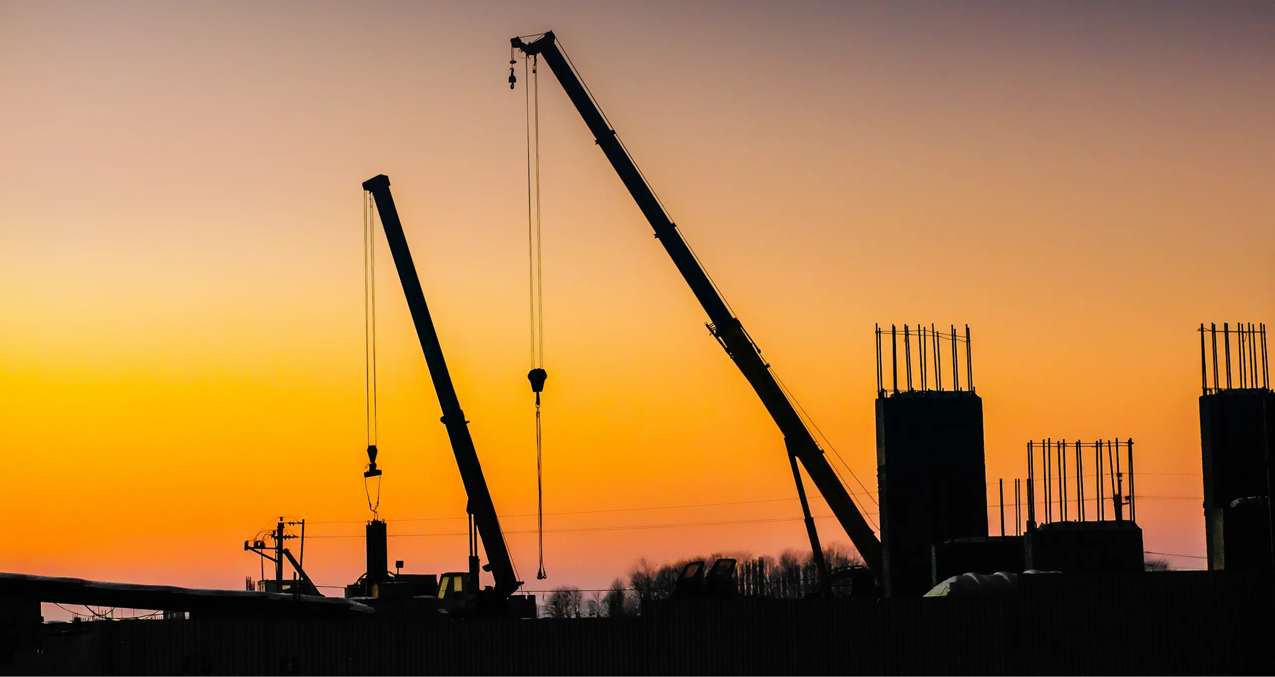 Vue au couché du soleil de deux grues et d'une structure en construction.